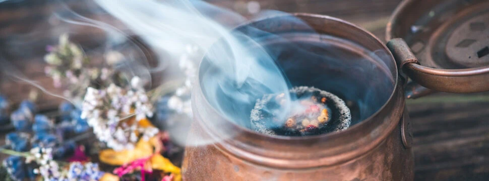 TCM Liestal | Getrocknete Kräuter, Blüten und Weihrauch auf einer Räucherkohle in einem Räuchergefäß aus Kupfer-Spirituelle Reinigung